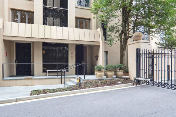 Front view of a modern multi-story building entrance with large windows and a gated driveway.