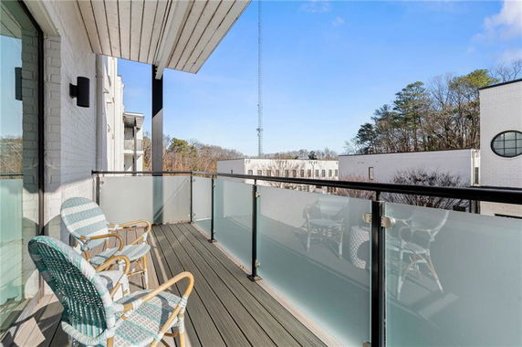 View from a balcony with chairs, overlooking nearby buildings and trees.