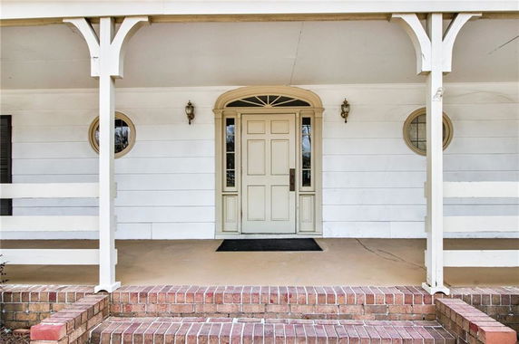 Front view of a house entrance with white siding, round windows, and decorative pillars.