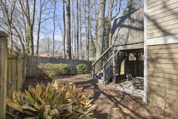 View of a fenced backyard area with outdoor stairs and trees.