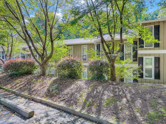 Front view of a two-story house partially obscured by trees and shrubs.