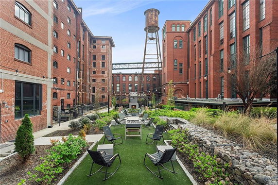 Courtyard view between large brick buildings with a garden and seating area.