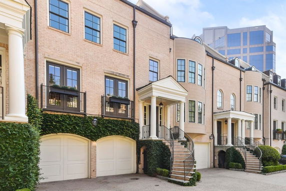 Front view of a row of elegant multi-story townhouses with arched garages and decorative columns.