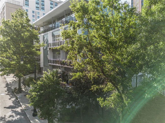Front view of a multi-story building with balconies and large windows partially obscured by trees.