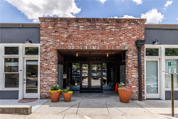 Front view of a brick building with glass doors and large potted plants on either side.