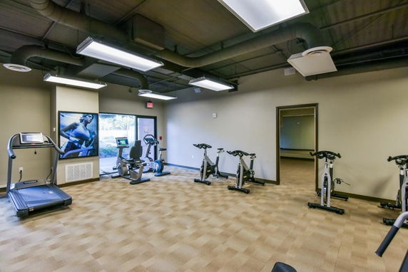 Indoor gym area with exercise machines and large windows.