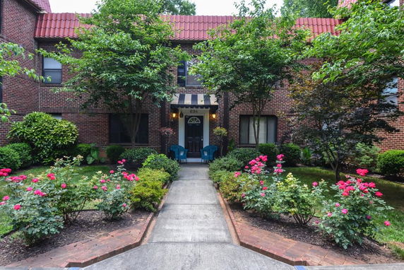 Front view of a brick building with a central entrance and a pathway lined with flowers and bushes.