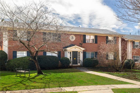 Front view of a two-story brick apartment building with shrubs and a tree in front.