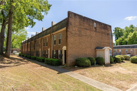 Side view of a multi-story brick townhouse with multiple units and a pathway along the side.