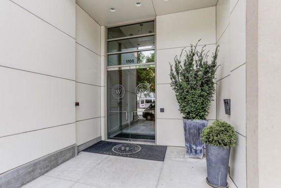 Entrance of a modern building with glass doors and plants.