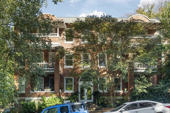 Front view of a three-story brick building with balconies and trees.