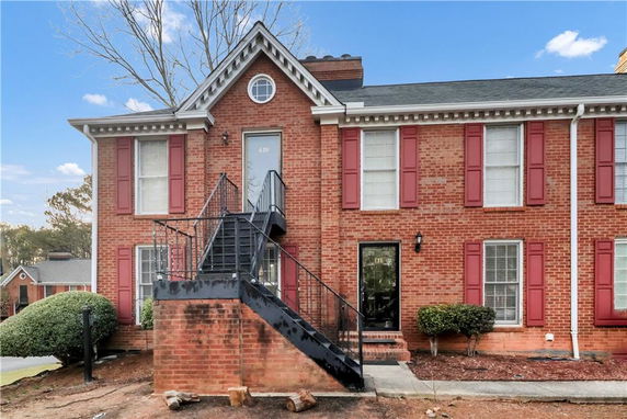 Front view of a two-story brick house with exterior stairs and red shutters.
