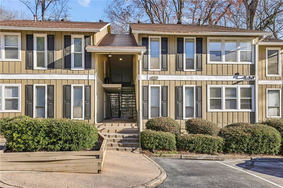 Front view of a two-story residential building with beige siding and black shutters.