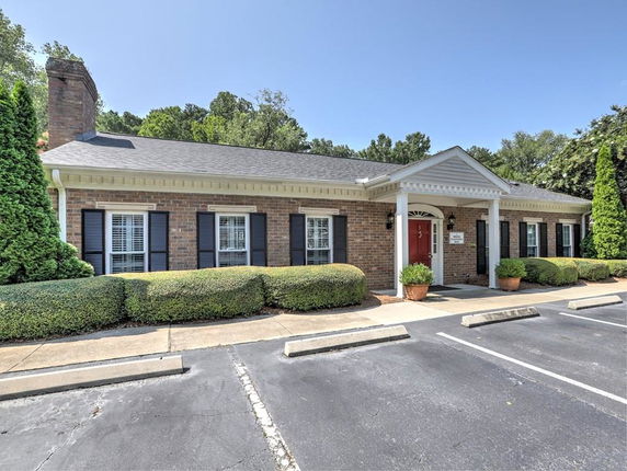 Front view of a single-story brick building with white columns and a red door.