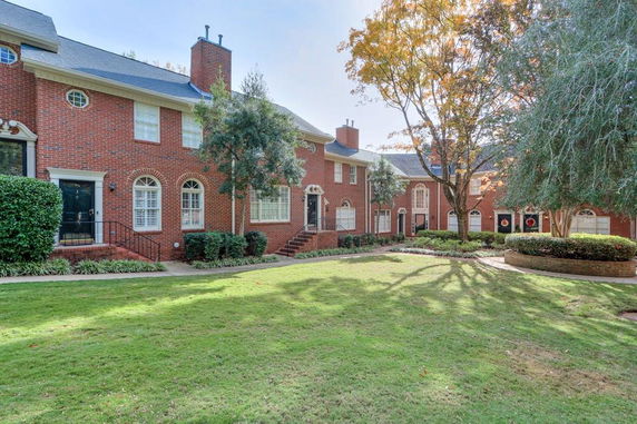 Front view of a row of two-story brick townhouses with white-framed windows and greenery in front.