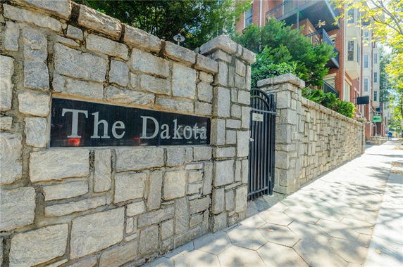Stone wall with a metal gate and a sign reading 'The Dakota' at the entrance of a building.