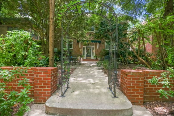 Front view of a house with a brick pathway, surrounded by greenery and a metal arch.