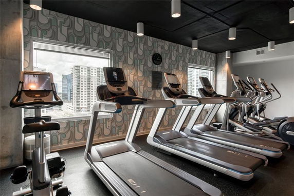 Indoor gym area with several treadmills and exercise equipment, overlooking a cityscape from large windows.