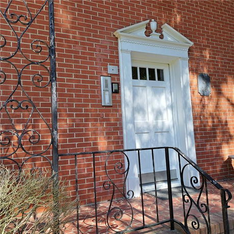 Front view of a brick house entrance with a white door and decorative wrought-iron railing.