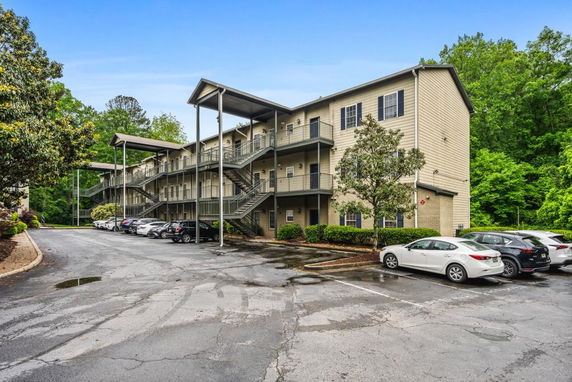 Front view of a multi-story apartment building with exterior staircases and a parking area in front.