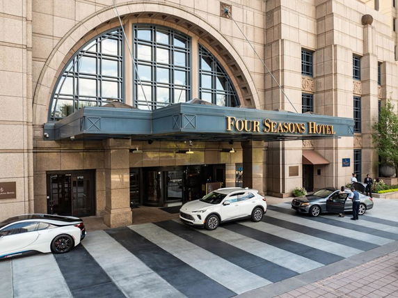 Front view of a hotel entrance with arched windows and vehicles parked at the entrance.