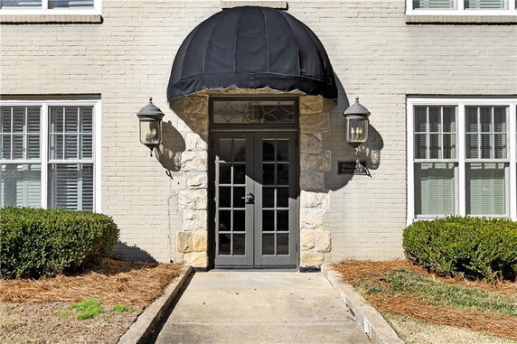 Exterior entrance of a building with a black awning and two large windows on each side.
