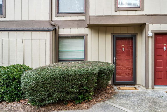 Front view of a beige townhouse with red doors and windows.