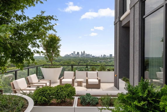 Outdoor terrace with seating area overlooking a city skyline and greenery.