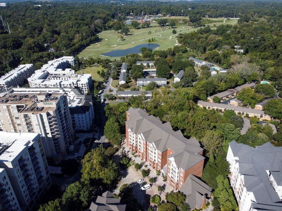 Aerial view of a residential area with high-rise buildings surrounded by greenery and a golf course in the background.