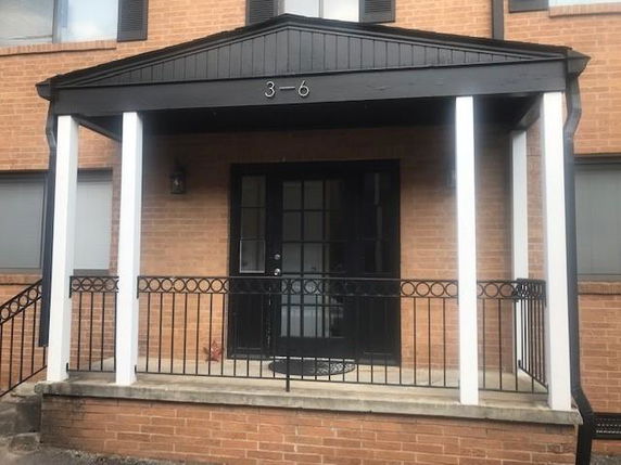 Front view of a brick building entrance with a covered porch and glass door.