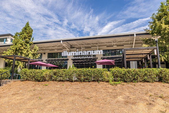 Front view of a modern building with an overhanging roof and outdoor seating area.