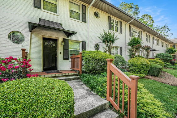 Front view of a multi-story brick townhouse with shrubbery.