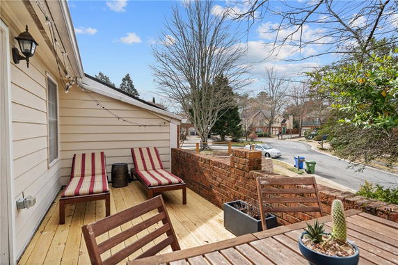 Rooftop with wooden deck and seating area, including lounge chairs and a table with potted plants.