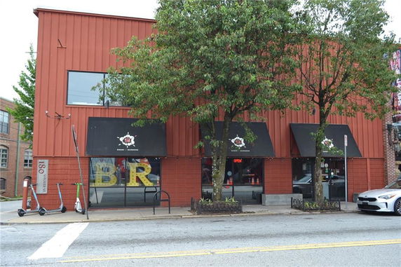 Front view of a two-story building with red exterior and black awnings, located on a street with scooters and a car parked nearby.