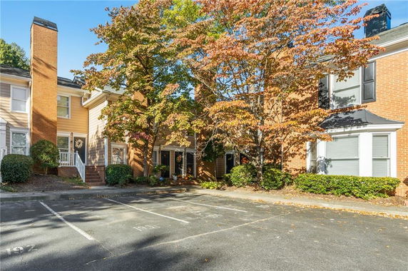 Outdoor parking area in front of a brick townhouse with trees.