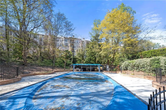 Outdoor area with a covered swimming pool surrounded by trees and a fence.