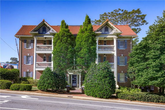Front view of a multi-story brick building with balconies and a red tile roof.