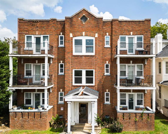 Front view of a multi-story brick apartment building with balconies.