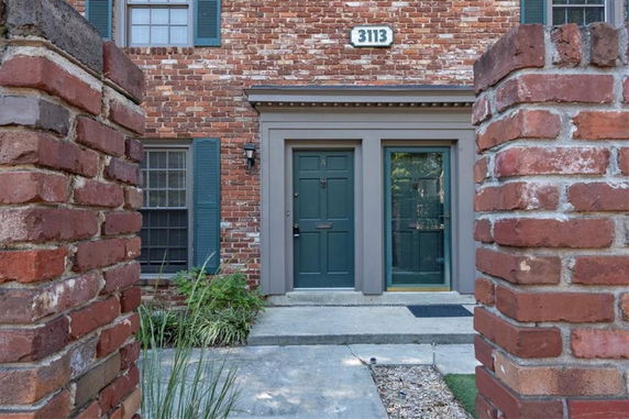 Front view of a brick house with a green door and a window with shutters.