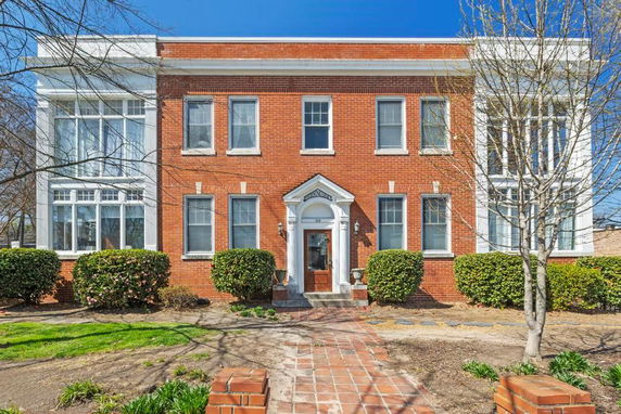 Front view of a two-story brick house with large windows and a central entrance.