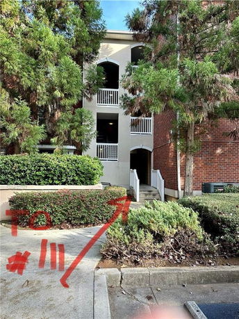 Front view of a multi-story building with stairs leading to entrances and a red brick wall on one side.