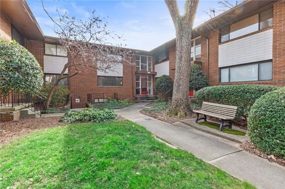 Front view of a two-story brick building with large windows and a bench in a landscaped area.