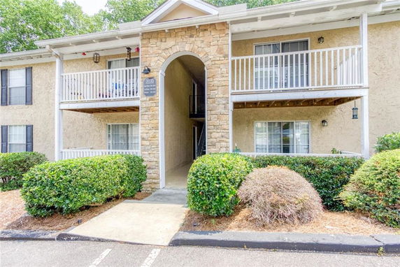 Front view of a two-story apartment building with balconies and a stone archway entrance.