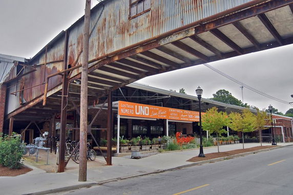 Front view of a rustic building with a metal and brick structure, featuring a large sign advertising a taco restaurant.