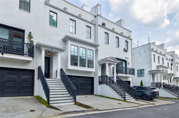 Front view of a multi-story townhouse with garage and stairs leading to the entrance.