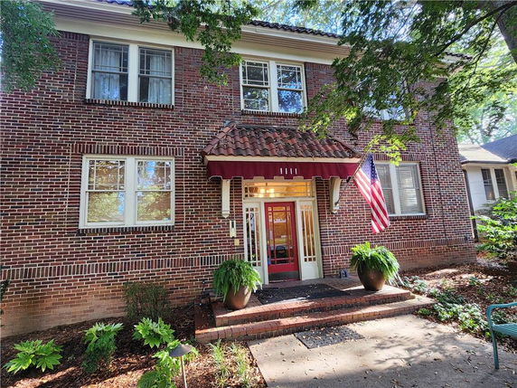 Front view of a two-story brick house with an entrance awning and American flag.