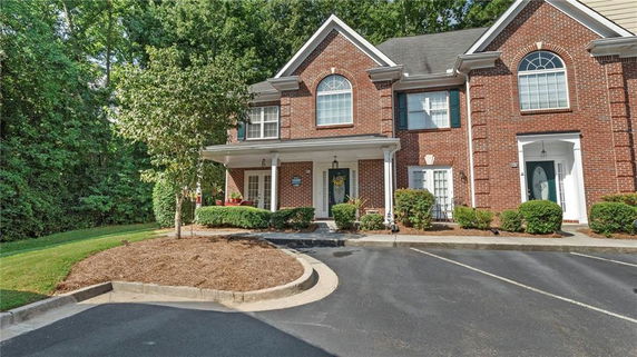 Front view of a two-story brick townhouse with arched windows and a landscaped front yard.