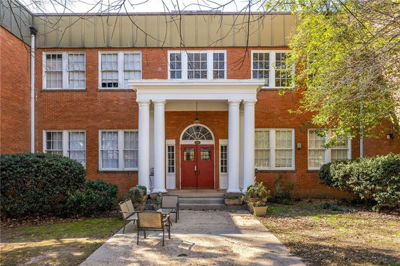 Front view of a two-story brick building with a central entrance featuring white columns and a red door.