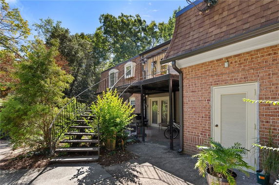 View of a two-story house with a staircase leading to an upper deck and visible brick exterior.