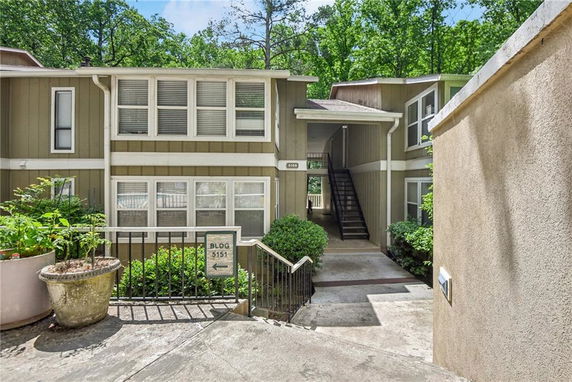 Front view of a multi-story apartment building with outdoor stairs and surrounding greenery.